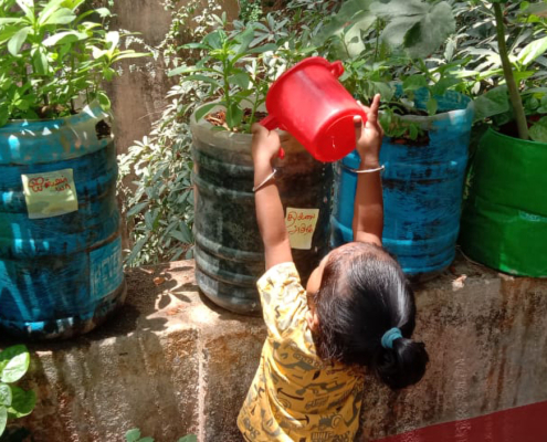 A young beneficiary watering her recycled container vegetable garden